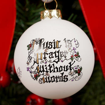 Decorative Christmas ornament with 'Music is prayer without words' text on a tree.
