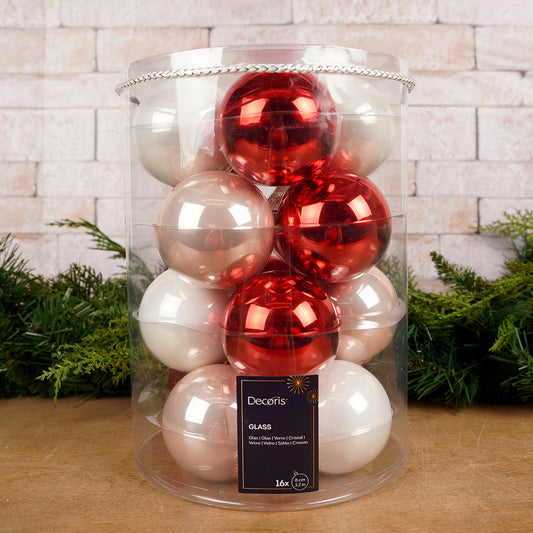 Clear cylindrical container filled with red and white Christmas ornaments on a wooden surface with a brick wall background.