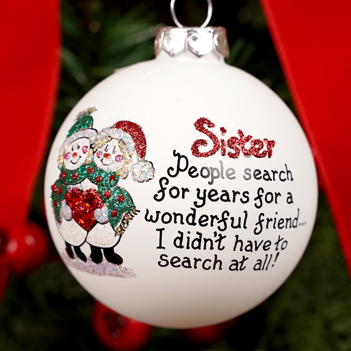 Christmas ornament with text and sister snowman illustration, hanging against a red background.