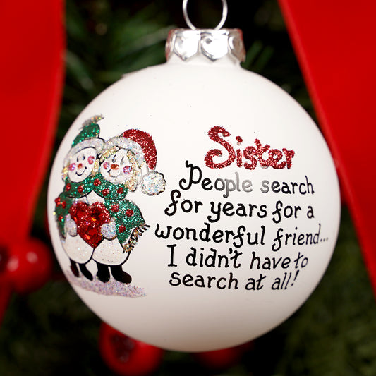 Christmas ornament with text and sister snowman illustration, hanging against a red background.