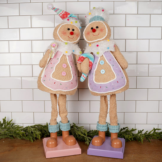 Two decorative gingerbread figures with colorful outfits against a white tiled wall.