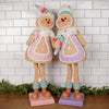 Two decorative gingerbread figures with colorful outfits against a white tiled wall.