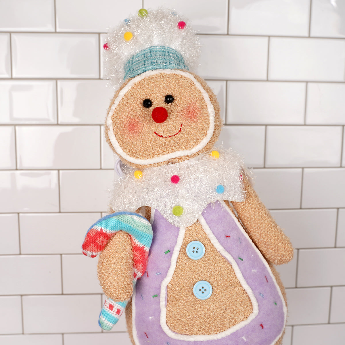 Toy gingerbread man with colorful buttons and scarf against a tiled wall background