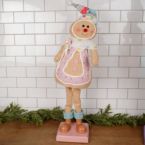 Christmas Place Decorative gingerbread man figurine with a pink apron against a white tiled wall.