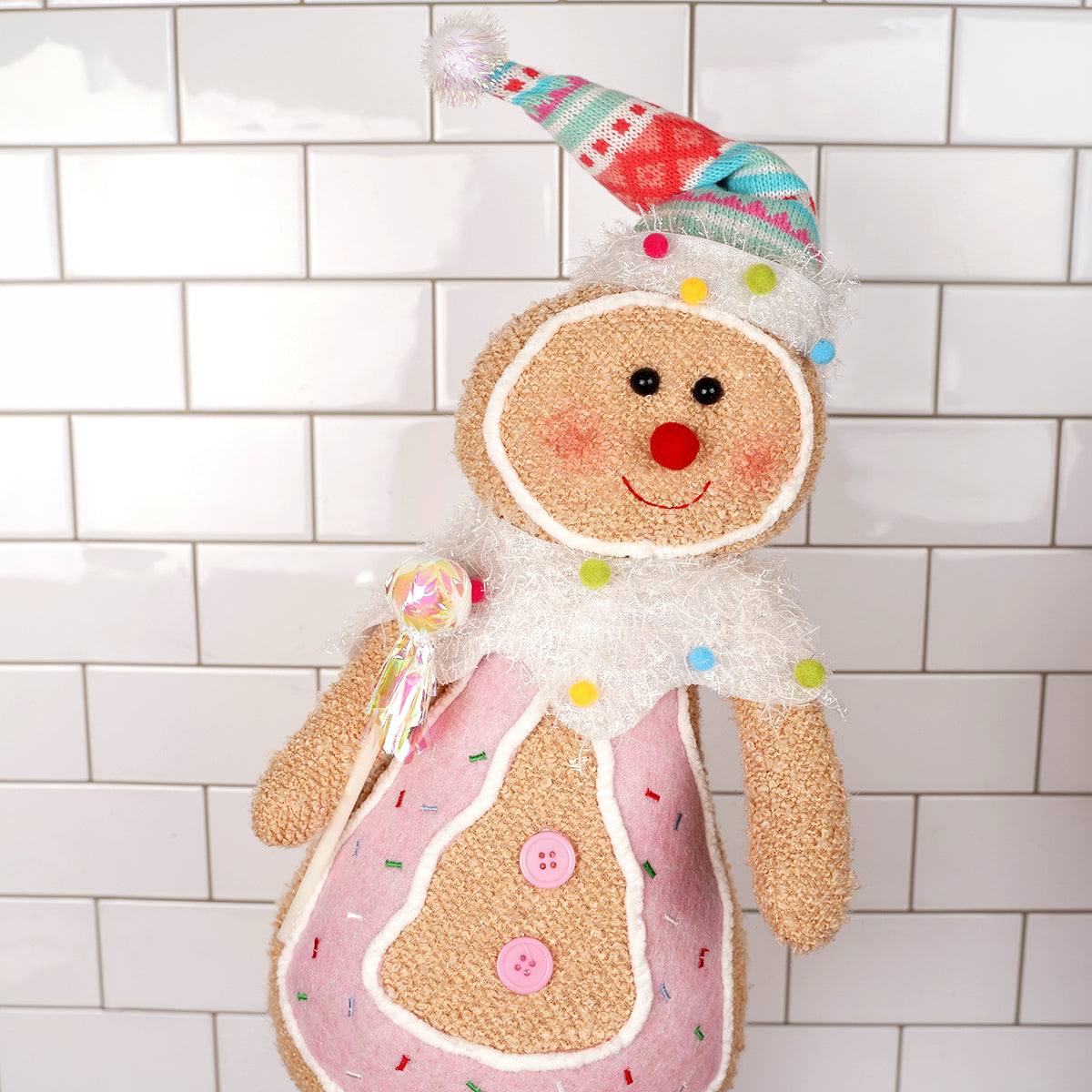 Plush gingerbread man toy with a colorful hat on a tiled wall background