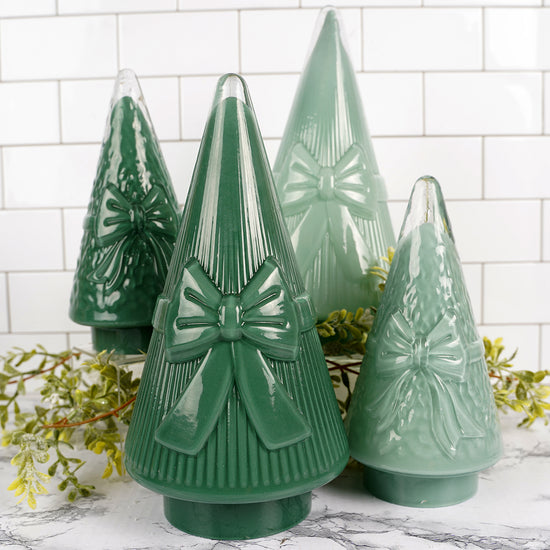 Set of green ceramic Christmas trees with bow details on a marble surface.