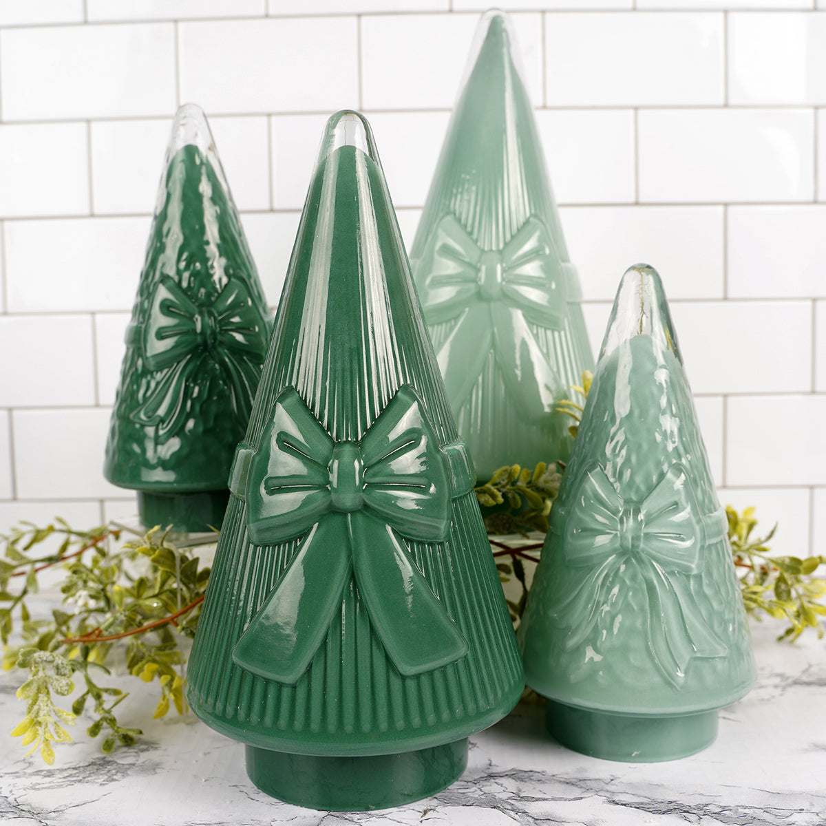 Set of green ceramic Christmas trees with bow details on a marble surface.