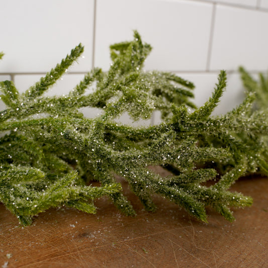 Greenery with snow on a wooden surface against a tiled wall background
