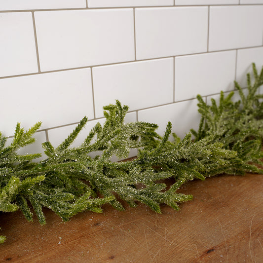 Artificial green garland on a wooden surface with a tiled wall background
