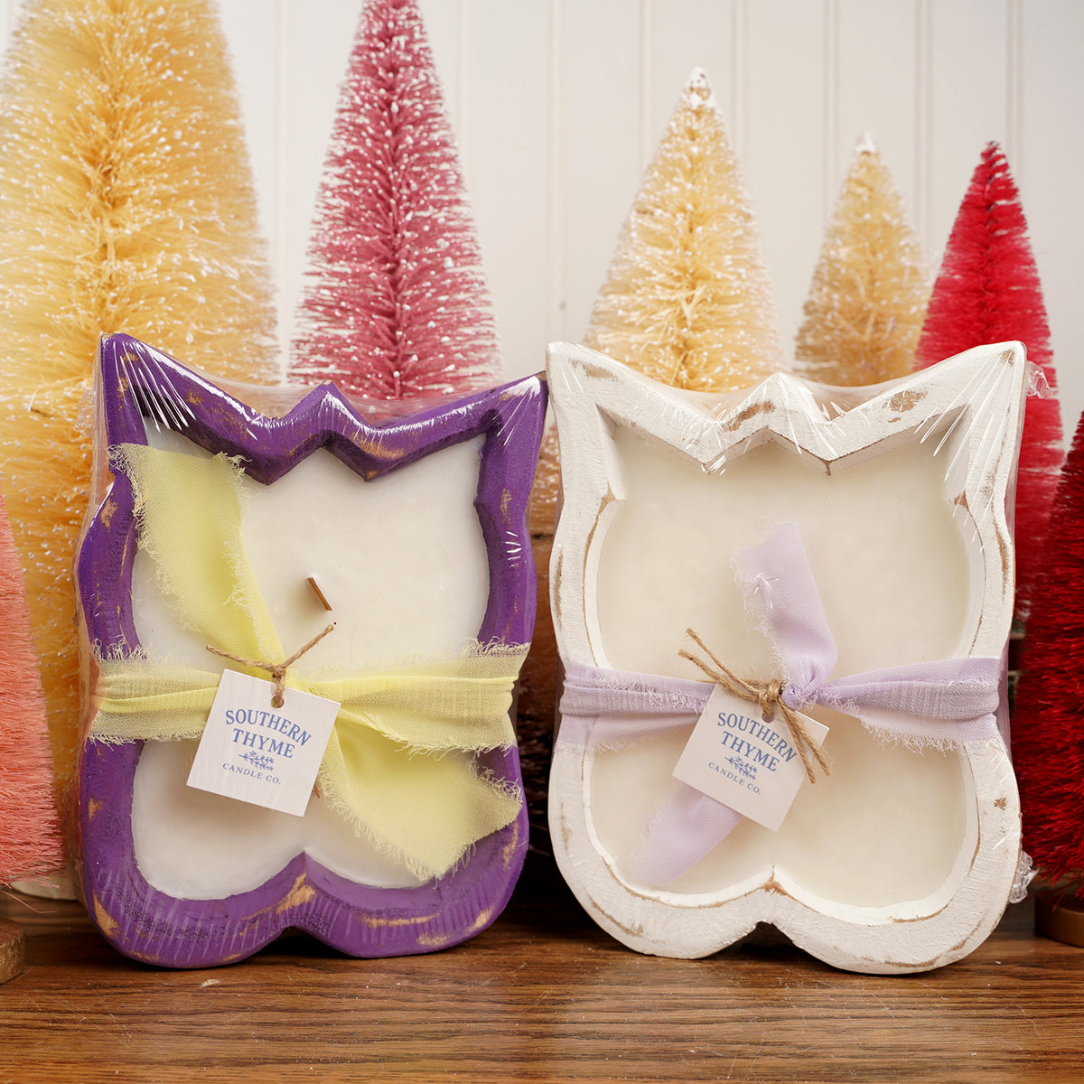 Two butterfly-shaped candles in packaging with Christmas trees in the background