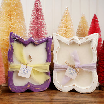 Two butterfly-shaped candles in packaging with Christmas trees in the background