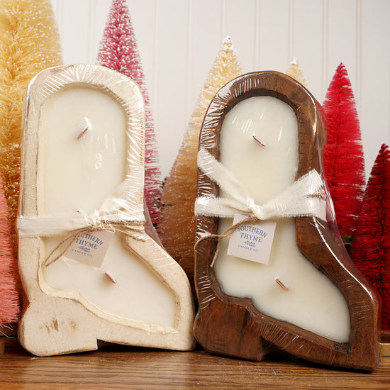 Two candles in wooden boot molds with decorative trees in the background
