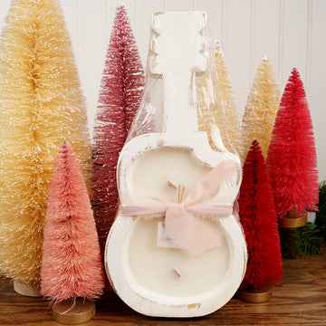Decorative candle with a bow in a guitar holder surrounded by small Christmas trees.
