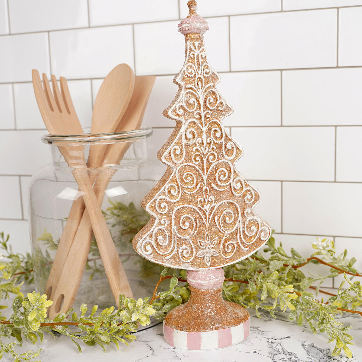 Decorative Christmas tree with pink and white pattern on a kitchen counter with utensils and greenery.