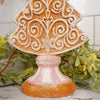 Decorative Gingerbread Christmas tree ornament with intricate white designs on a pink base, surrounded by greenery.