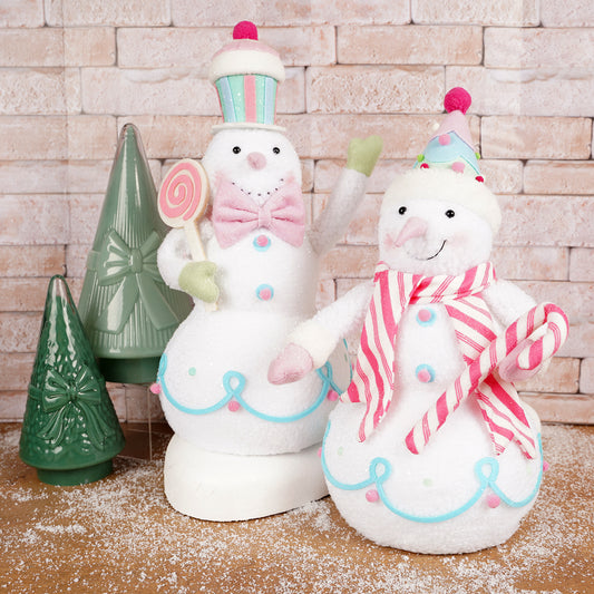 Two decorative snowmen with candy-themed outfits against a brick wall.