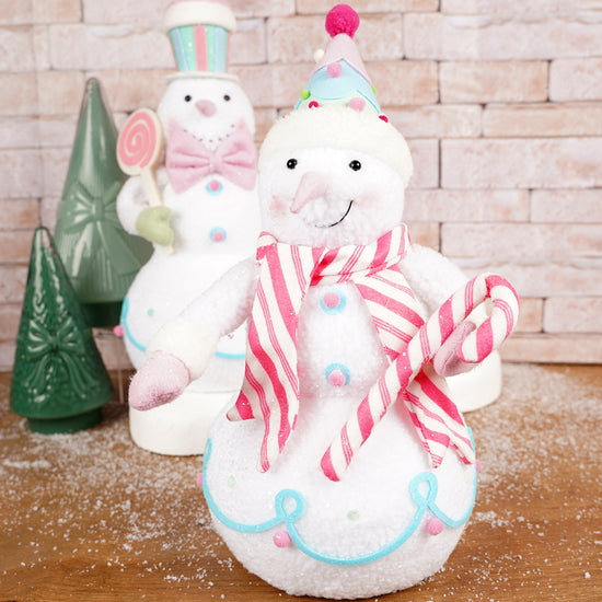 Decorative snowman figurines with candy cane scarf and hat on a wooden surface.